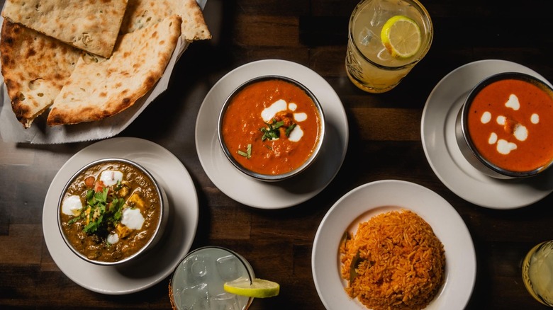 Assortment of Indian dishes, rice, naan, and drinks on wooden table