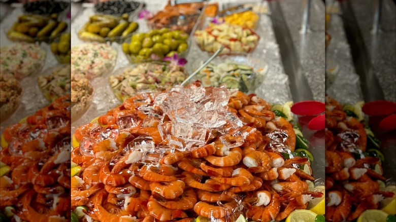 Pile of ice-covered shrimp on the buffet table with blurred dishes in background