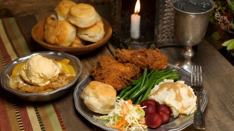 Rustic table setting with plate of fried chicken and sides, cobbler, and biscuits