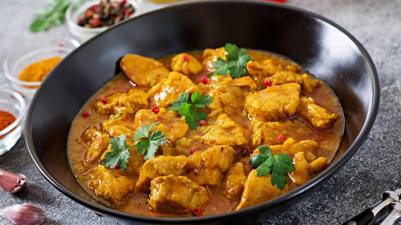 Chicken curry in black dish with blurred spices