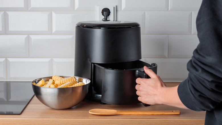 An unbranded air fryer in use with a bowlful of uncooked french fries by the side