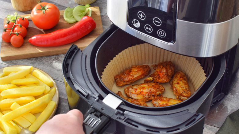 An unbranded air fryer shown open with cooked chicken inside and a variety of uncooked food surrounding it