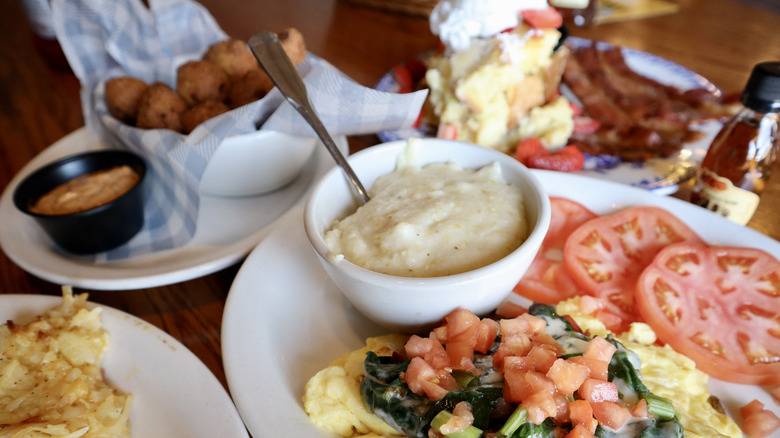 plates of tomatoes, eggs, grits, and more on a wood table