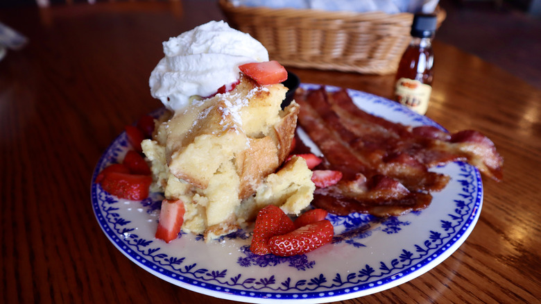 Cracker Barrel French toast with strawberries and cream next to bacon on plate