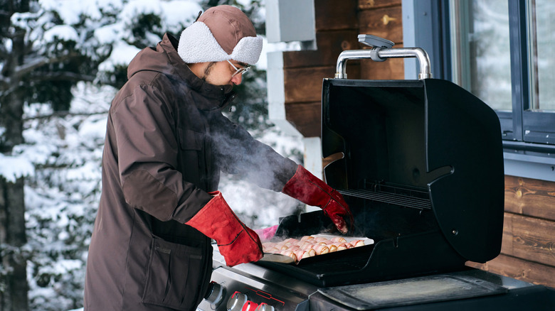 Guy in coat grills outside in winter