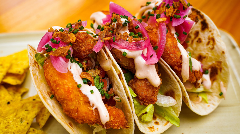 Three fish tacos and tortilla chips on a plate