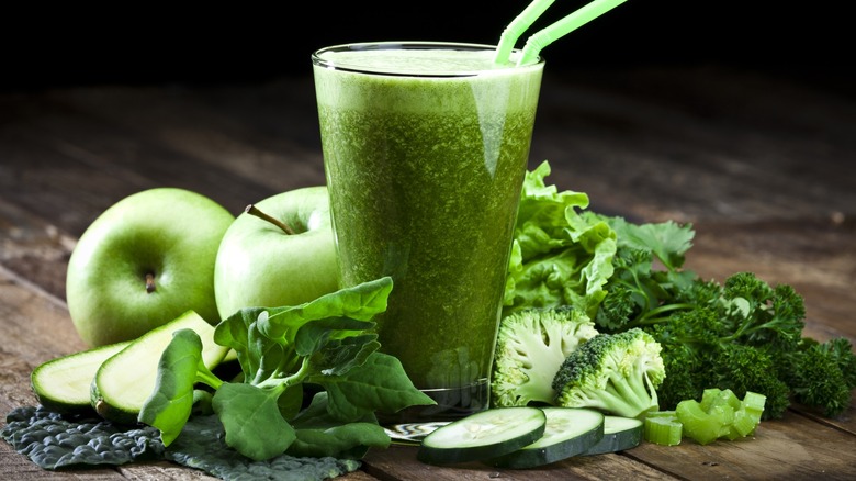 A pint glass of green juice next to various ingredients