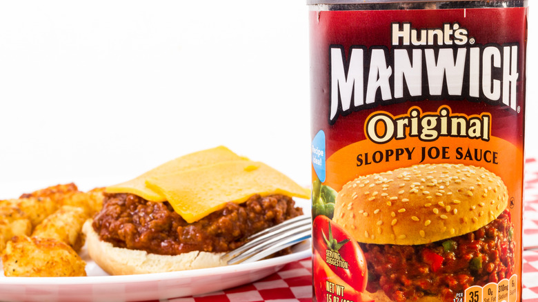 A homemade sloppy Joe with cheese and tater tots on a white plate next to a can of Hunt's Manwich Sloppy Joe Sauce