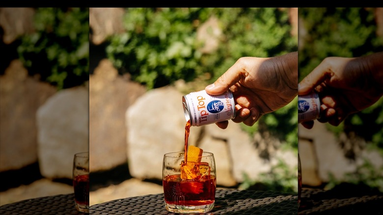 Person pouring Tip Top Proper Cocktails Negroni into stemless wine glass