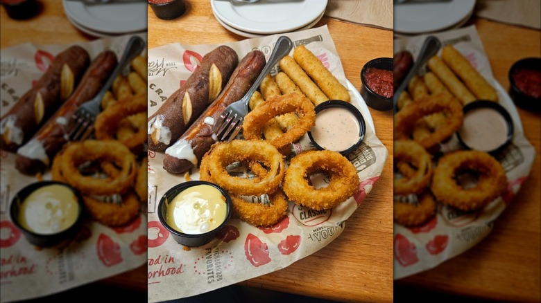 Dining table at Applebee's showing Ultimate Trio appetizer with pretzel sticks, mozzarella sticks, onion rings, and 2 dips, with mirror border