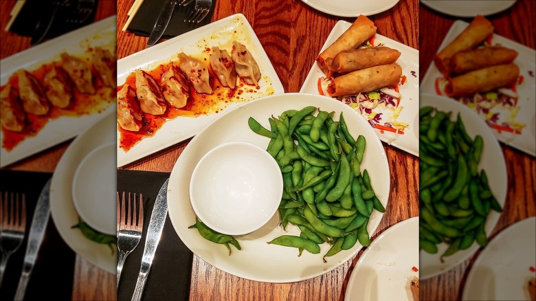 Dining table at P.F. Chang's with 3 plates of edamame, dumplings, and spring rolls appetizers, with a mirror border