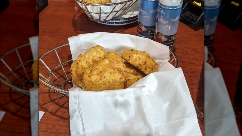 Red Lobster Cheddar Bay Biscuits in a metal bread basket on top of white cloth, on a wood dining table with mirror border