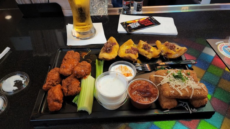 A black dining table at TGI Fridays with an appetizer platter of wings, potato skins, mozzarella sticks, and dips, with a beer and napkins