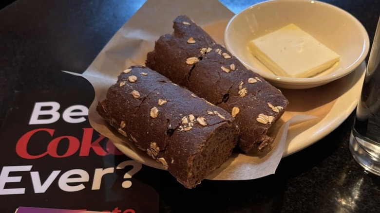 2 long pieces of Cheesecake Factory brown bread with butter on a table on top of a menu
