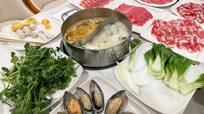Two-compartment hot pot with plates of raw meat and mussels on table at Happy AYCE Hot Pot