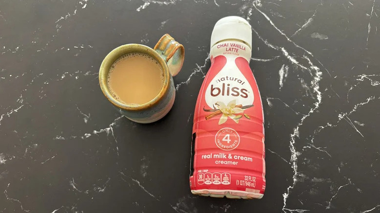 A carton of Natural Bliss Chai Vanilla Latte Creamer on a kitchen counter next to a cup of coffee