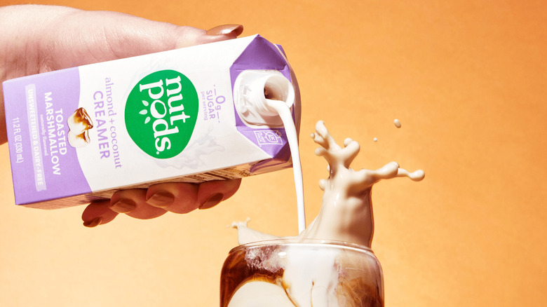 A close-up of a woman's hand pouring nutpods Toasted Marshmallow Creamer into a glass of iced coffee