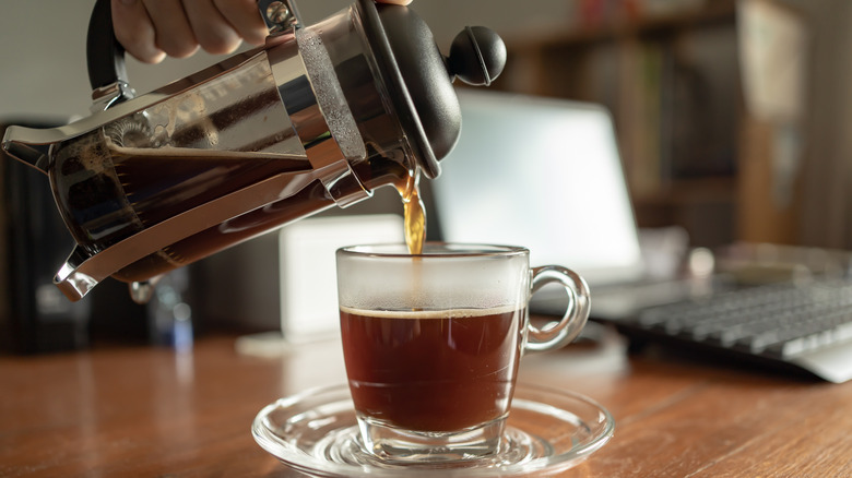 Someone pouring coffee from a French press into a cup