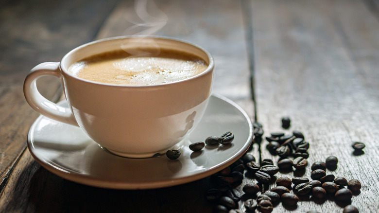 A steaming cup of coffee next to scattered beans