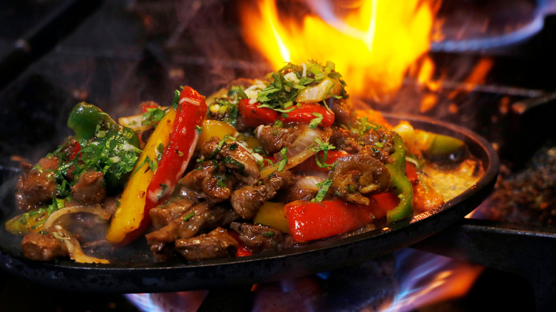 a beef fajita on its sizzler plate, cooking over the open flame of a gas stove