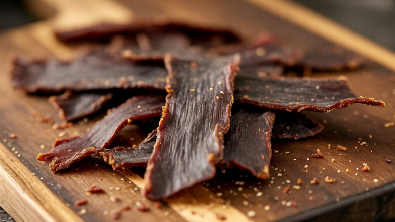 close-up image of thin-sliced beef jerky on a wooden cutting board, with a dusting of spices visible around it