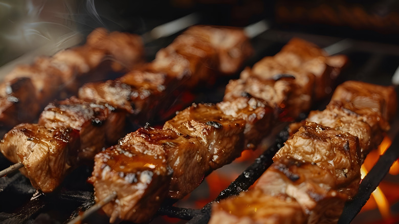 four skewers of beef kebabs cooking on a grill over the coals