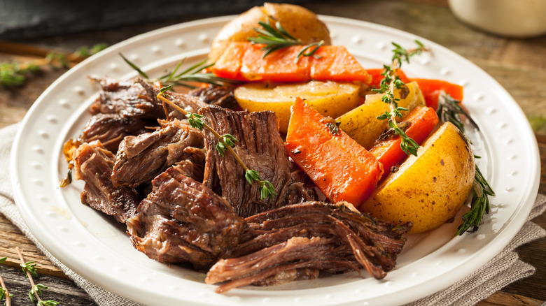 pot roast with carrots and potatoes, shown on a white plate with stems of thyme