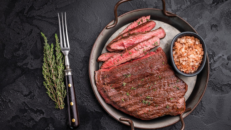cooked sirloin steak on serving pan with bowl of salt on black background