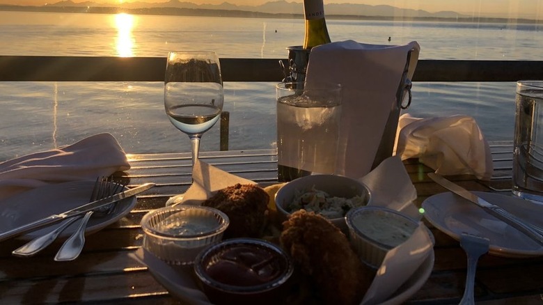 A plate of seafood and a glass of wine with water and the Olympic Mountains behind