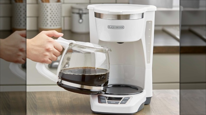 Hand grabbing carafe from white Black+Decker 12-cup digital coffee maker