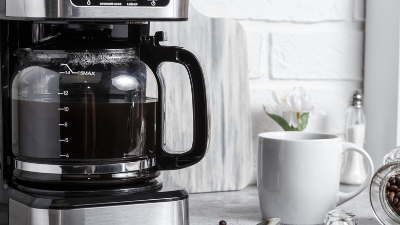 Drip coffee maker beside a white mug of coffee