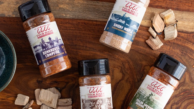Four bottles of Four Sixes seasoning blends on wooden table with pieces of wood