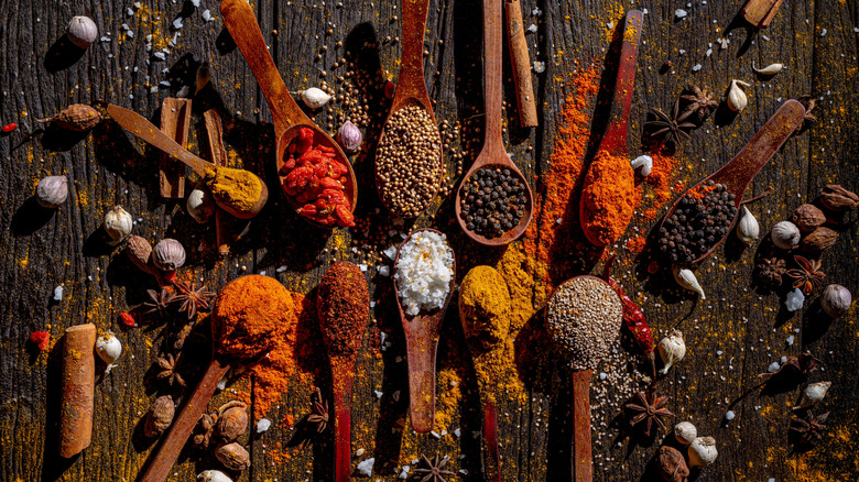 Assortment of various spices on wooden spoons on wooden table