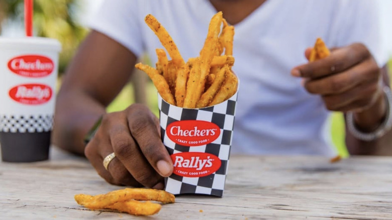 A person eating from a carton of Checkers and Rally's fries
