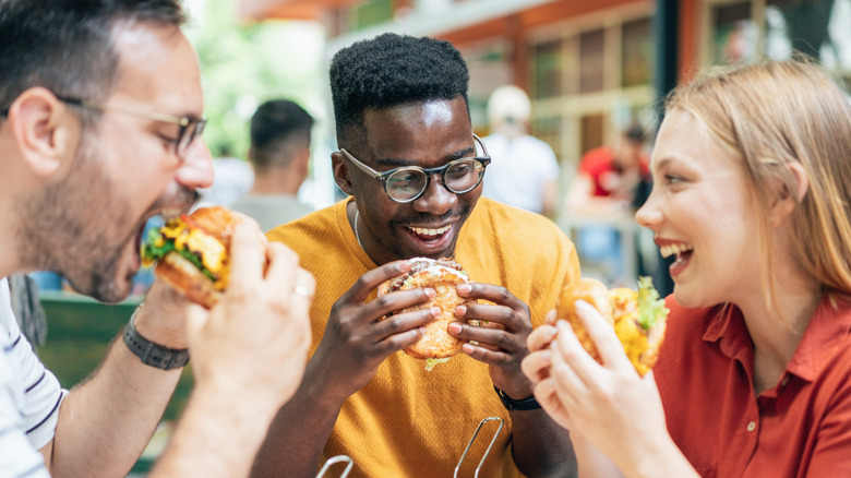 Three people eating fast food burgers at an outdoor table