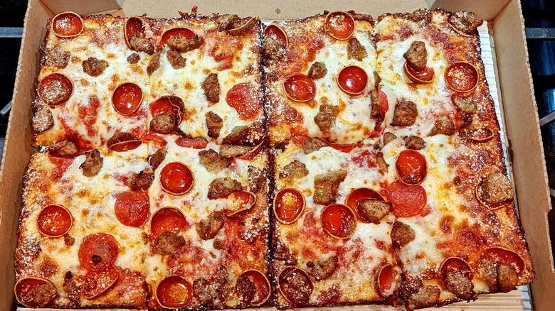 A box of Detroit-style deep dish pizza with pepperonis and sausage in a box
