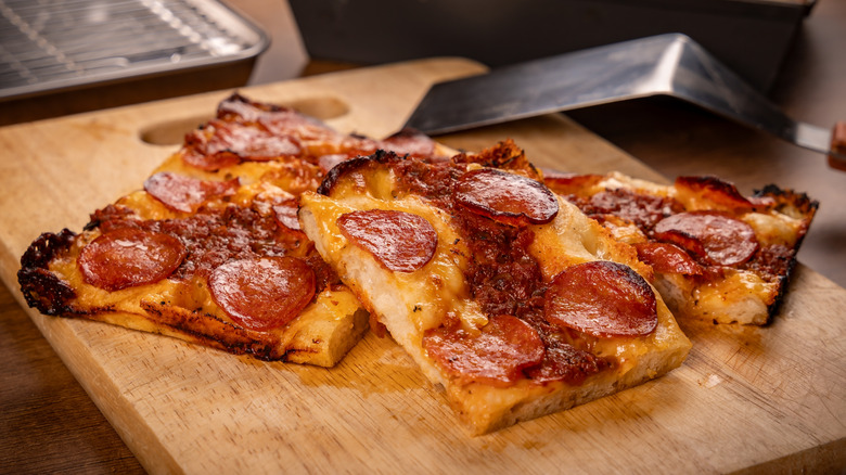 Stacked slices of Detroit-style pizza on a cutting board beside a spatula