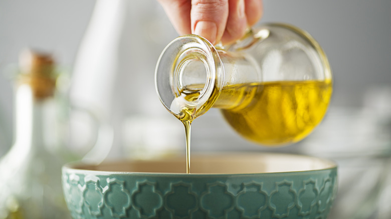 A clear glass just of olive oil being poured over a small bowl