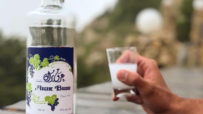 Hand holding arak glass next to a premium arak bottle