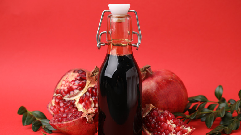 Pomegranate molasses or sauce with open pomegranates on red background