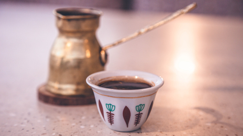 Traditional hand-painted Lebanese coffee cup with brass pot in background
