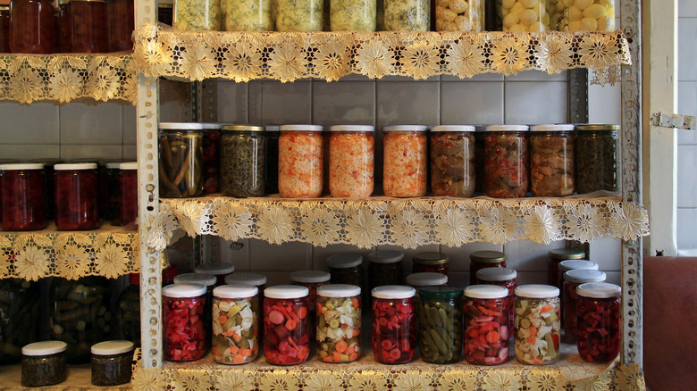 Pickled goods in glass jars on shelves lined with doilies