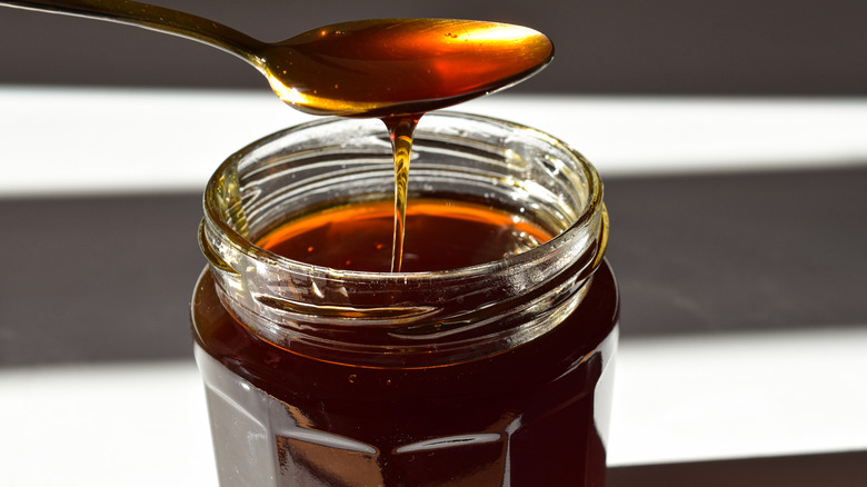 Dark honey scooped with a spoon from a glass jar