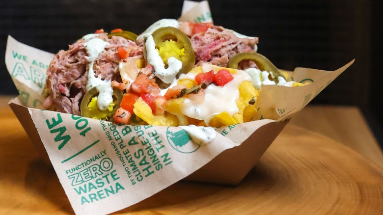 Loaded nachos with jalapeños and meat in paper tray