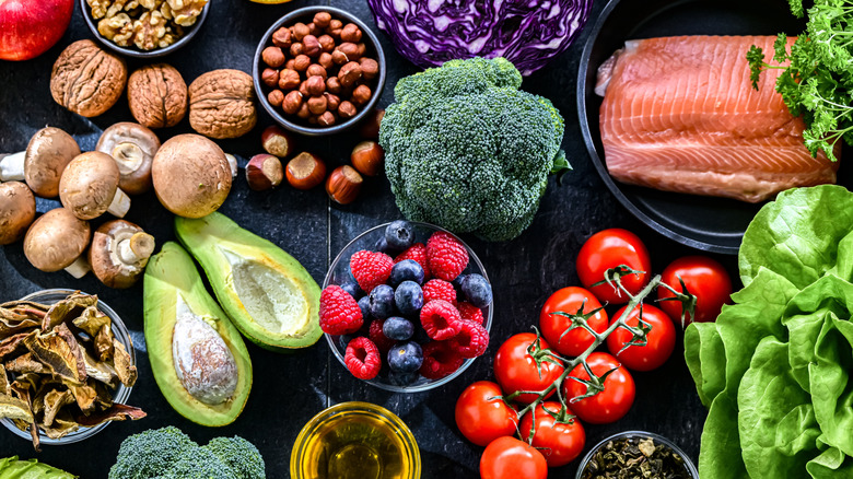 A spread of various fruits, vegetables, nuts, and a big piece of salmon all laid out on a black wooden surface.
