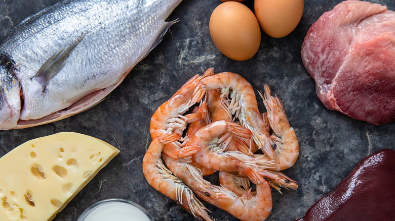 A spread of foods high in B12 including prawns, pork, liver, a whole fish, eggs, and a hunk of cheese.