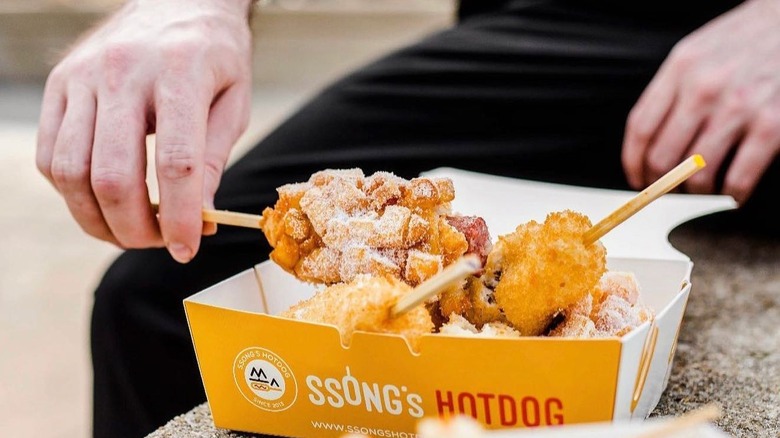 man holding ssongs hot dogs in take out container