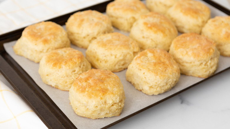 Baked buttermilk biscuits arranged in three rows on top of black tray lined with white parchment.