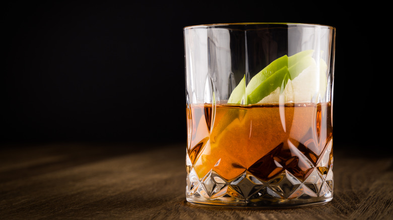 an old fashioned cocktail with a slice of green apple