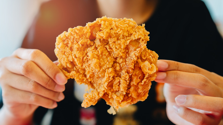 A woman holds a piece of fried chicken